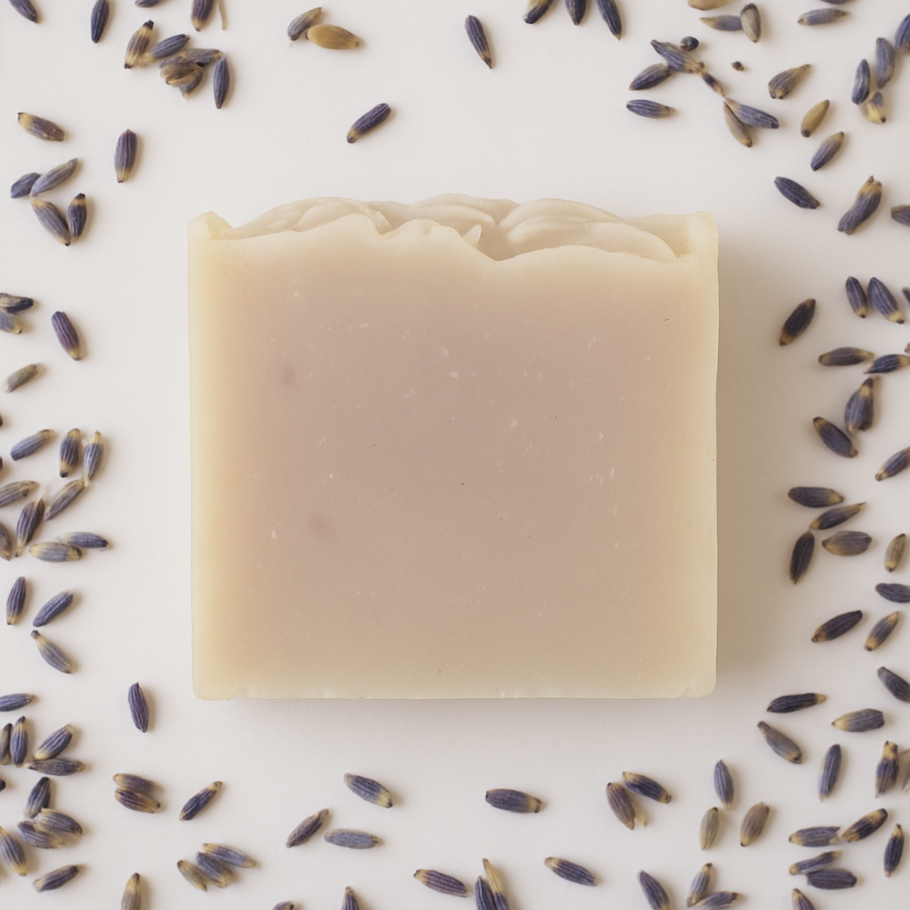 Bar of soap surrounded by lavender flowers on a light background